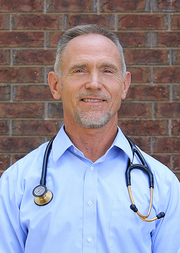 Dr. Stuart Porter DO, professional head shot smiling in front of red brick building