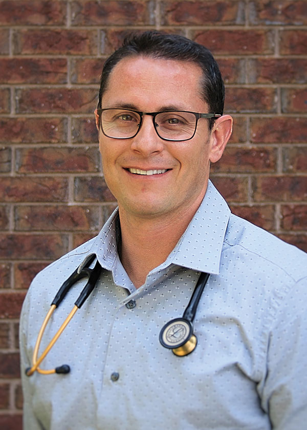 Cory Fowler smiling professional head shot in front of red brick building