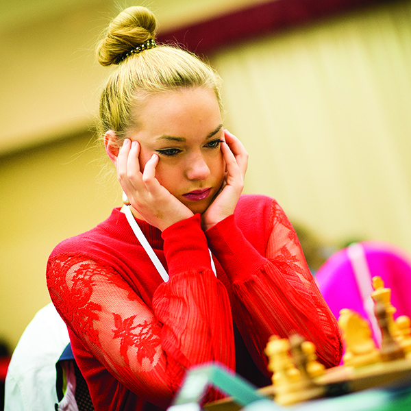 Serious woman wearing red shirt focused on chess board in deep thought