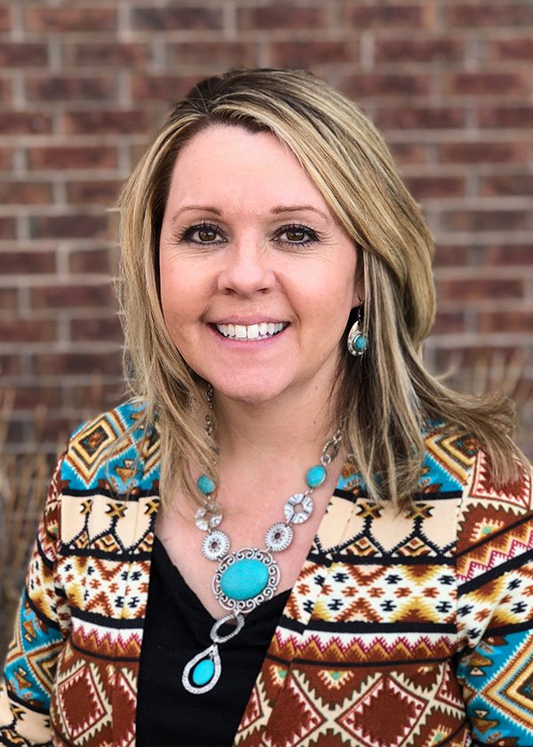 Linda Steele in black shirt and sweater smiling in front of red brick professional headshot