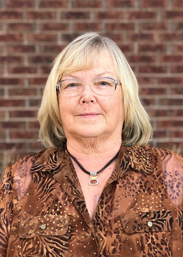 Maargaret Hawkins in brown blouse smiling in front of red brick professional headshot